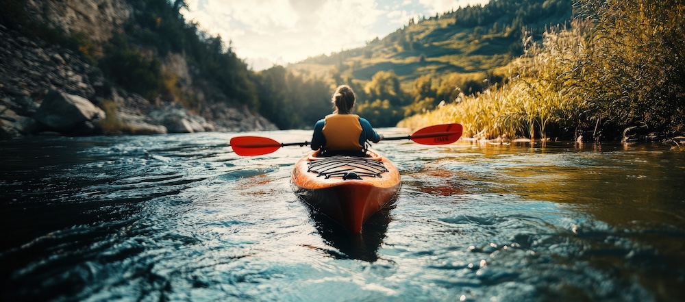 Person paddling a kayak down a flowing river surrounded by nature