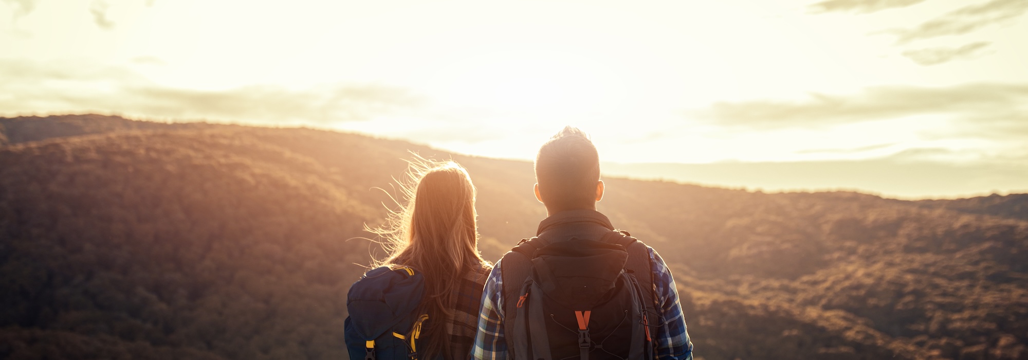Rear view of couple with backpacks hiking together in nature on autumn day.