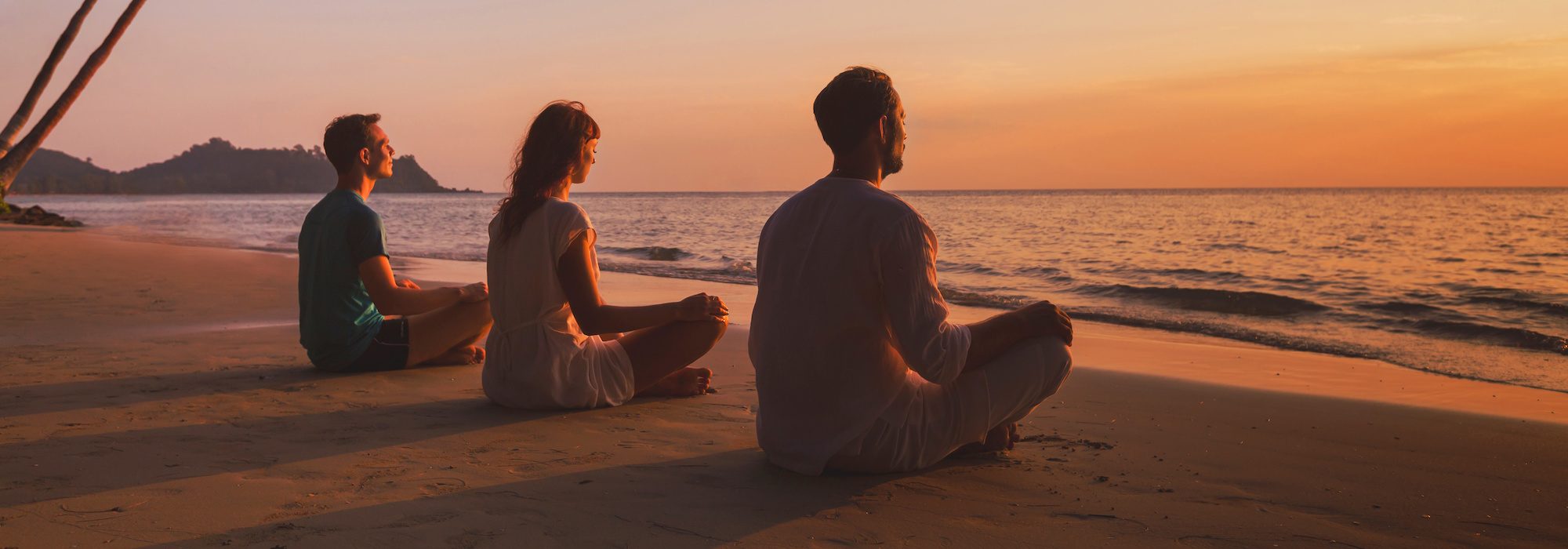 yoga retreat on the beach at sunset, silhouettes of group of people meditating