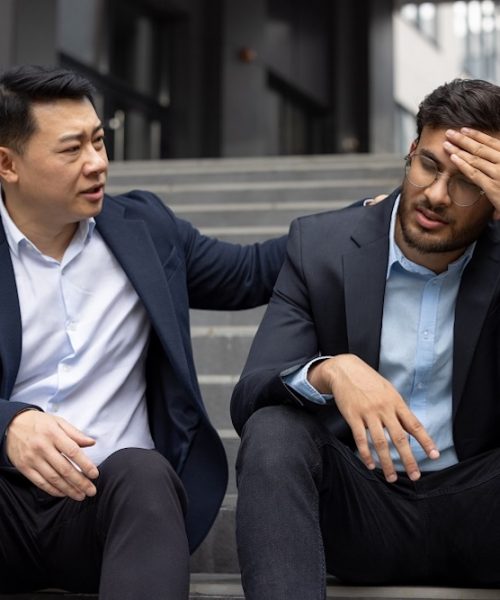 Business professional offering support to stressed colleague. Two men sit on office steps, one providing empathy and understanding during challenging work situation. Concept of support.