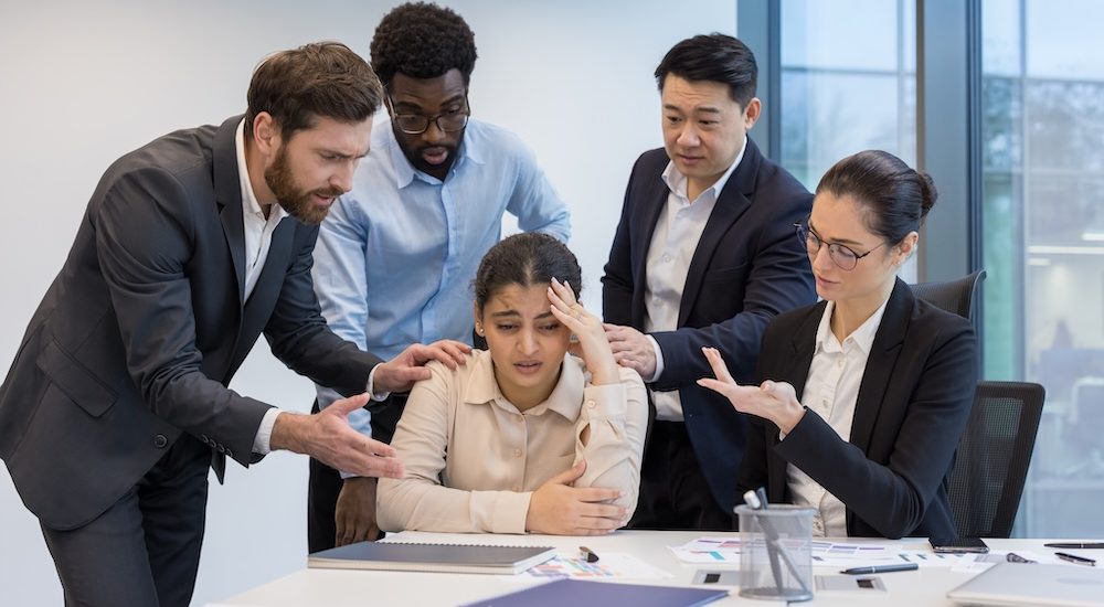 Colleagues support upset sad woman. Diverse business team at workplace comforting female employee.