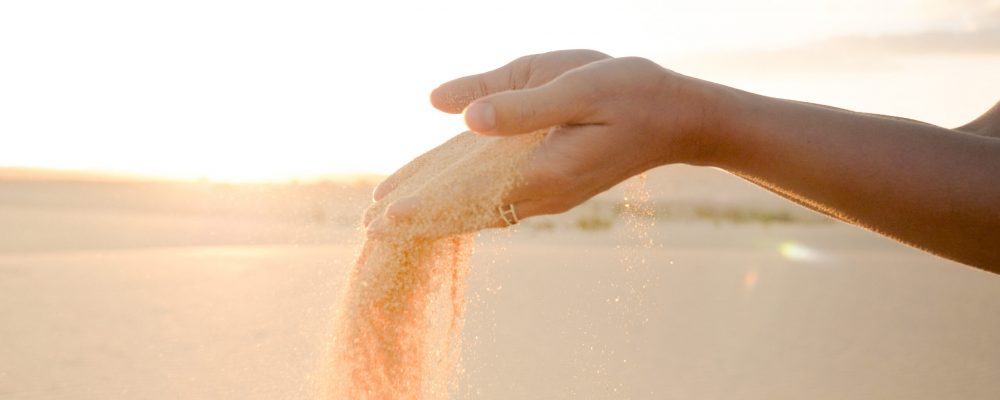 Closeup of young woman releasing sand from hands. Sand flowing with wind in desert at sunset. Wellness and relaxation concept.