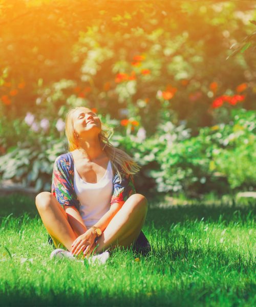 Happy free young woman sitting outdoors in yoga position with closed eyes on summer park grass Calm girl enjoy smile and relax in spring city air. Mindset inner light peace concept. Bali asia sun joy