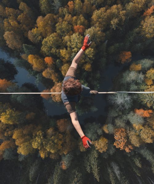 A breathtaking view of a tightrope walker walking along a line high above a beautiful forest. Topics of highline, longline, extreme activities. Top view.