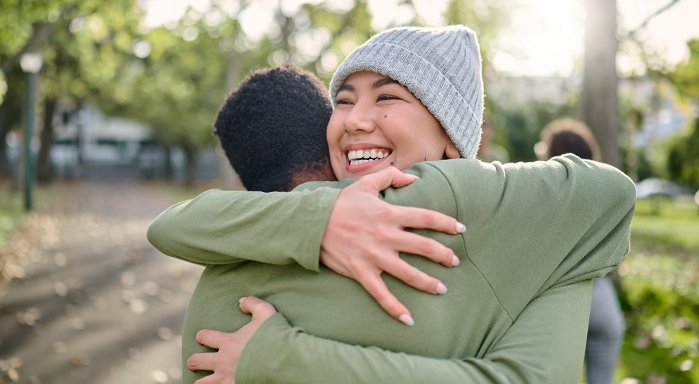 Friends, hug and smile for relationship, support or care embracing love, compassion or friendship in nature. Happy woman and man hugging, smiling and enjoying embrace in happiness for partnership.