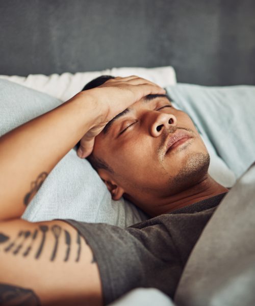 Tired, rest and sick man sleeping in the bedroom while in recovery or healing in his apartment. Burnout, illness and male person with a headache or fever taking a nap in bed at his modern home